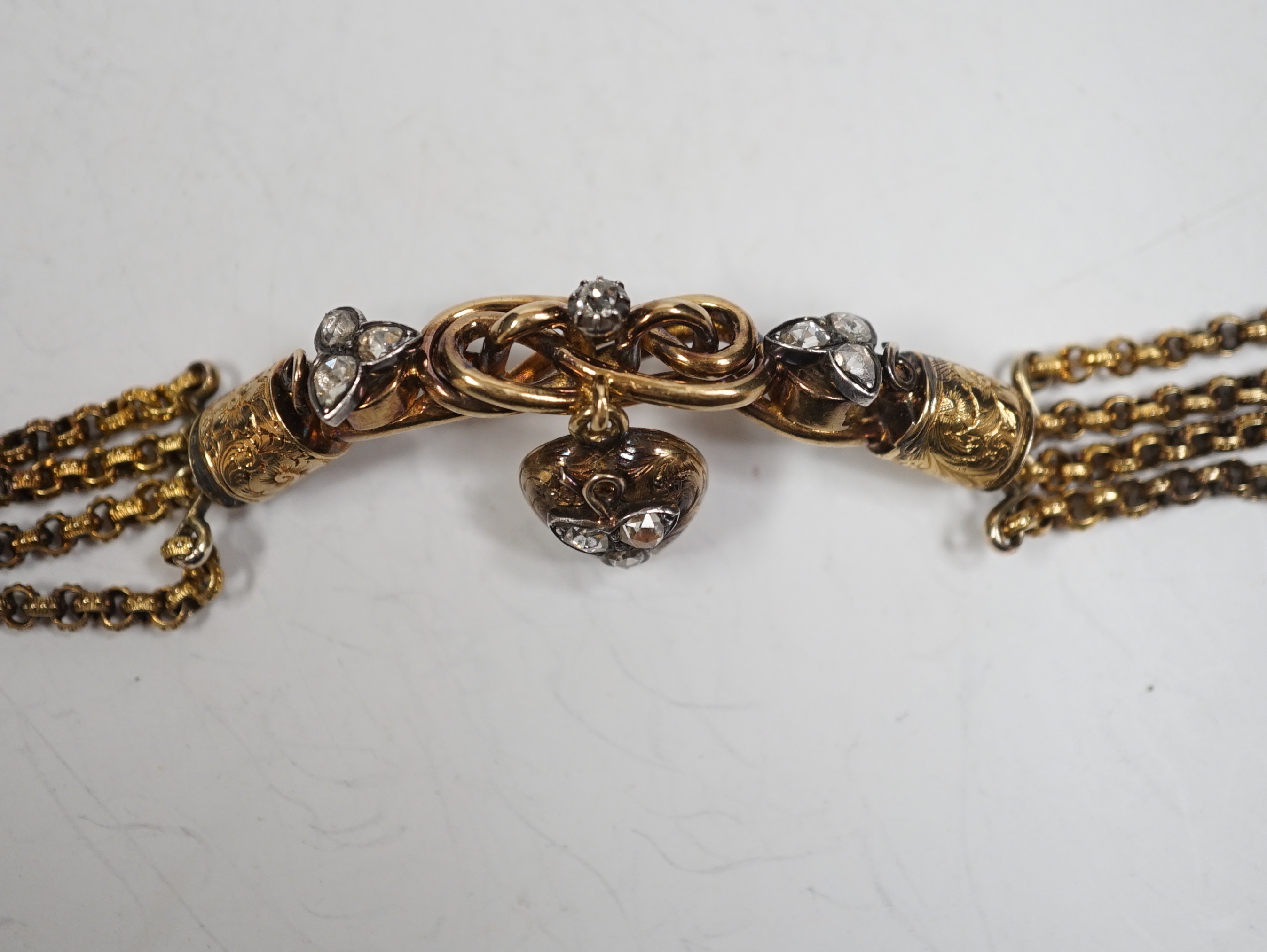 An antique yellow metal (test as 18ct) and rose cut diamond set triple strand bracelet, the central scrolling motif, hung with diamond set heart shaped charm, approx. 17cm, gross weight 30 grams.